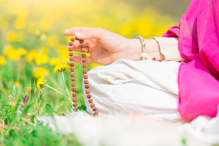 Woman reads the yoga mantra during practice with the mala on a flowery meadow in spring